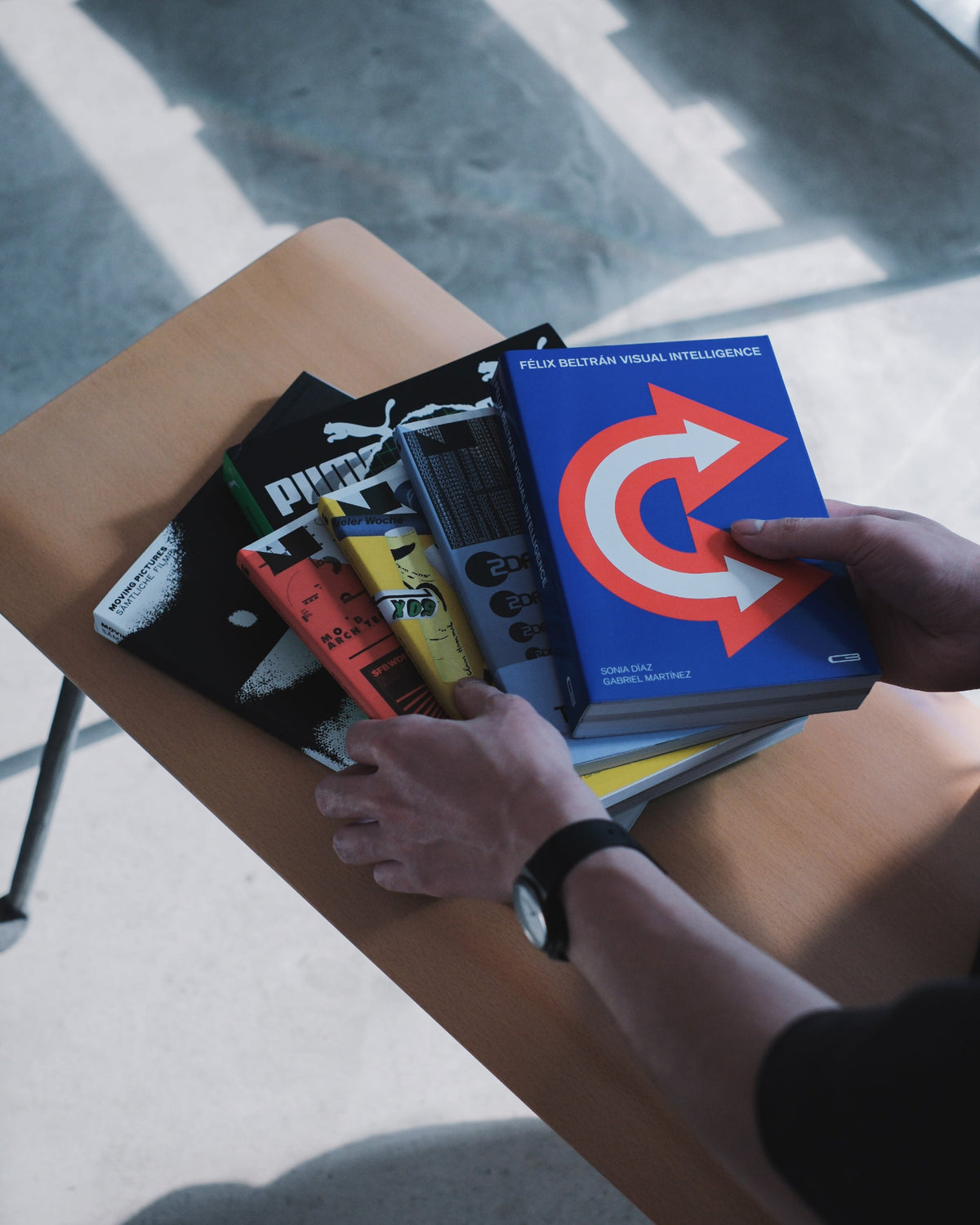 A stack of OPTIK BOOKS titles on a table, held in hand
